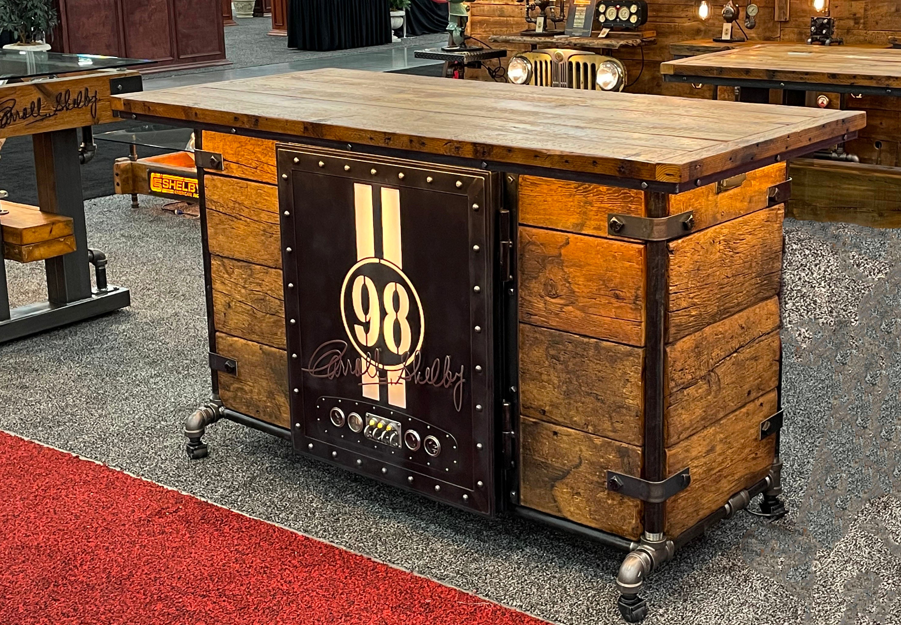 A large industrial-style bar made of barn wood with a hidden fridge and a Carroll Shelby door front, featuring LED lighting and stewert Warner gauges.